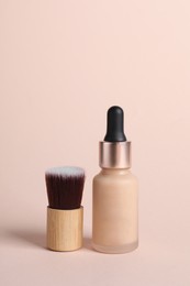 Bottle of skin foundation and brush on beige background. Makeup product