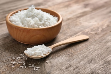 Photo of Bowl and spoon with fresh coconut flakes on wooden background