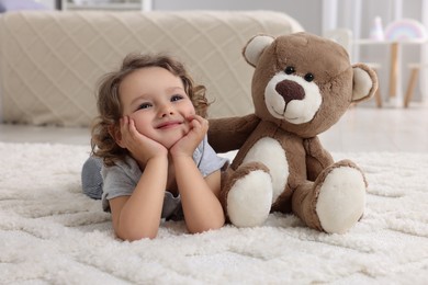 Photo of Cute little girl with teddy bear on floor at home