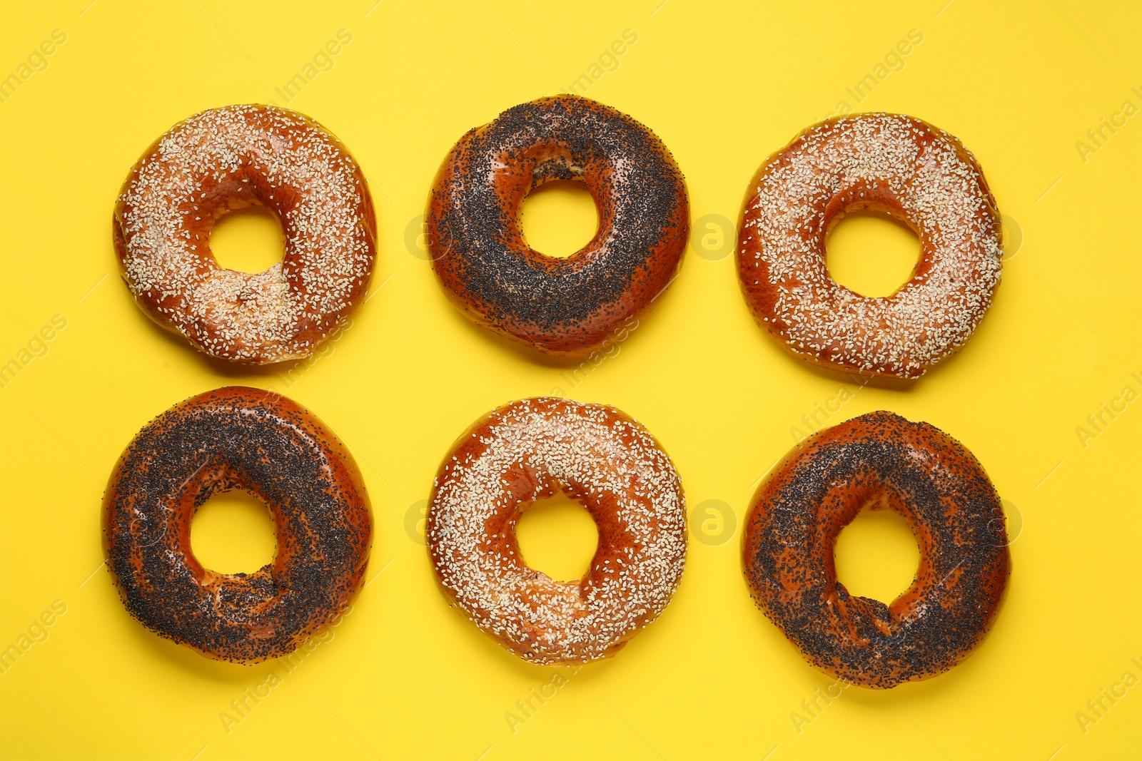 Photo of Many delicious fresh bagels on yellow background, flat lay