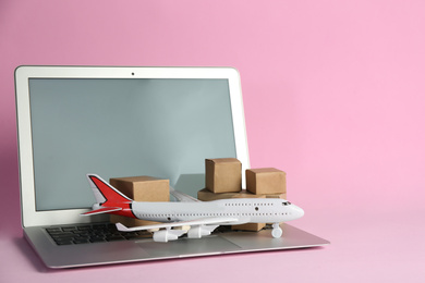 Laptop, airplane model and carton boxes on pink background. Courier service