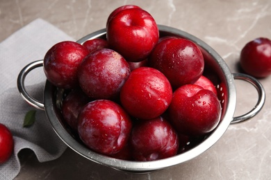 Delicious ripe plums in colander on grey marble table, closeup