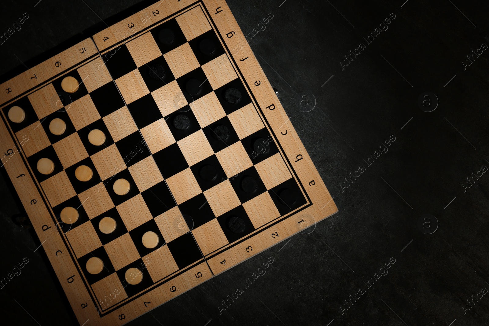 Photo of Wooden checkerboard with game pieces on black table, top view. Space for text