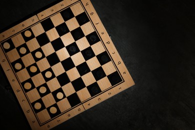 Photo of Wooden checkerboard with game pieces on black table, top view. Space for text