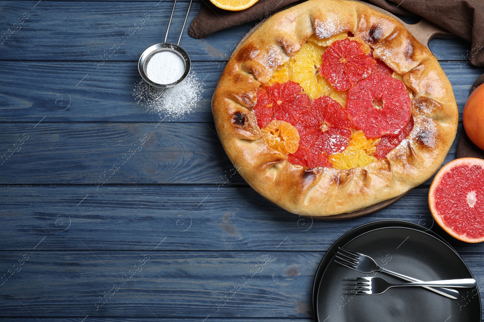 Photo of Delicious galette with citrus fruits served on blue wooden table, flat lay. Space for text