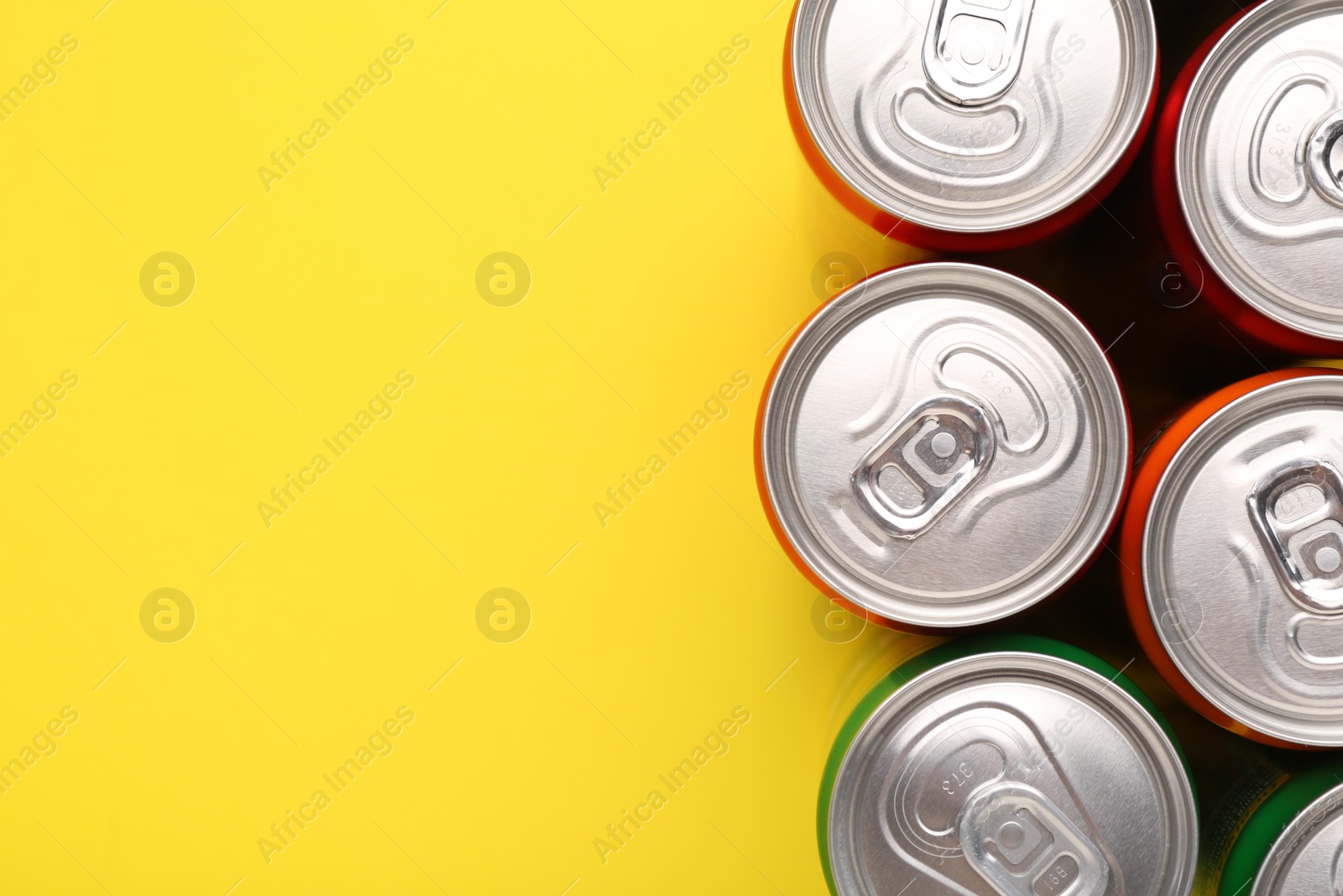 Photo of Energy drink in cans on yellow background, top view. Space for text