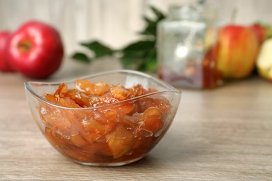 Photo of Tasty apple jam in glass bowl on wooden table, space for text