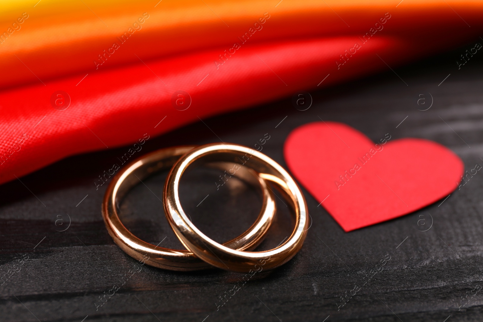 Photo of Rainbow LGBT flag, wedding rings and heart on black wooden background