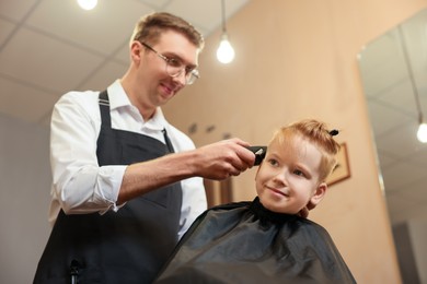 Professional hairdresser cutting boy's hair in beauty salon, low angle view