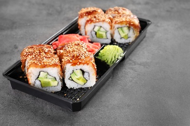 Box with tasty sushi rolls on grey table, space for text. Food delivery