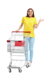 Young woman with empty shopping cart on white background