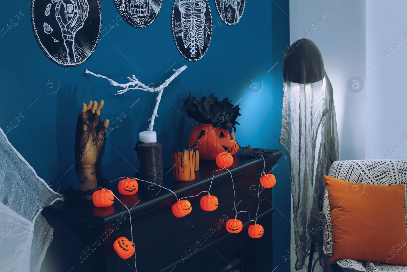 Photo of Jack-o'-lantern lights and different Halloween decorations on black fireplace near blue wall