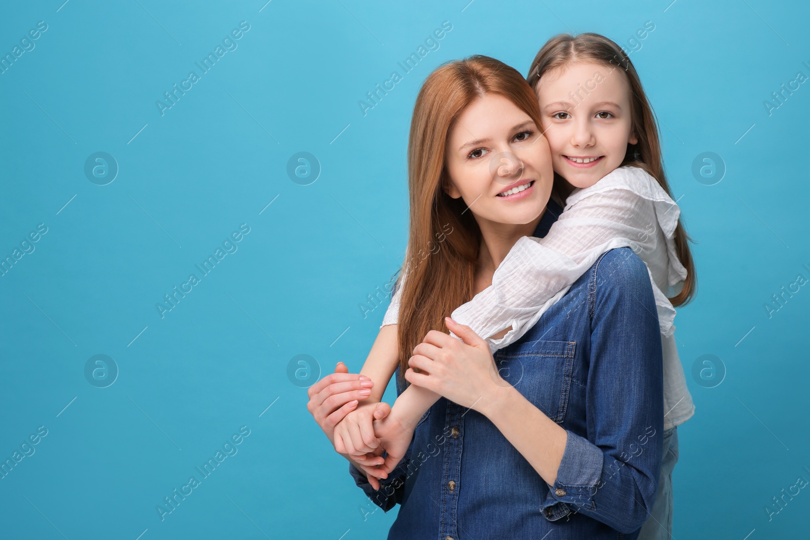 Photo of Portrait of happy mother and her cute daughter on light blue background. Space for text