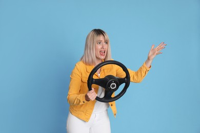 Photo of Emotional woman with steering wheel on light blue background