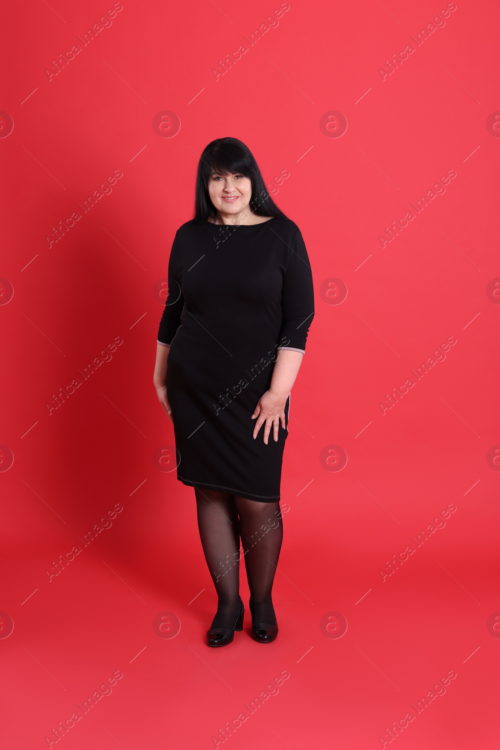 Photo of Beautiful overweight woman in black dress on red background