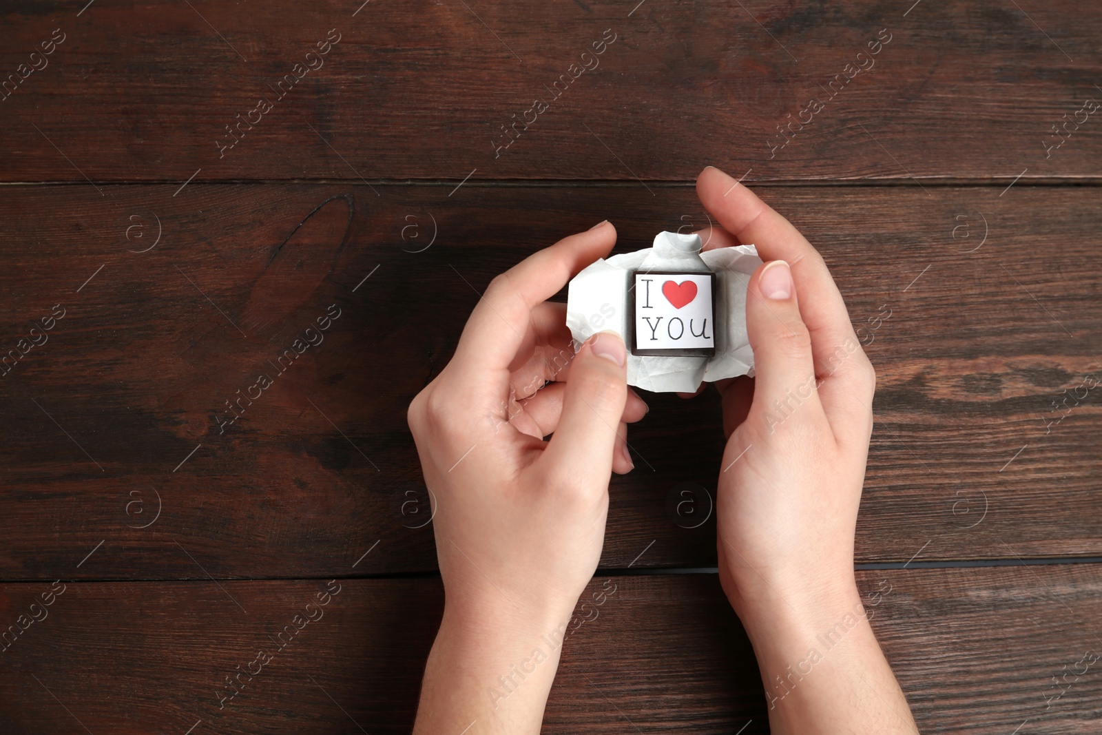 Photo of Woman holding chocolate candy with message I Love You on wooden background, top view