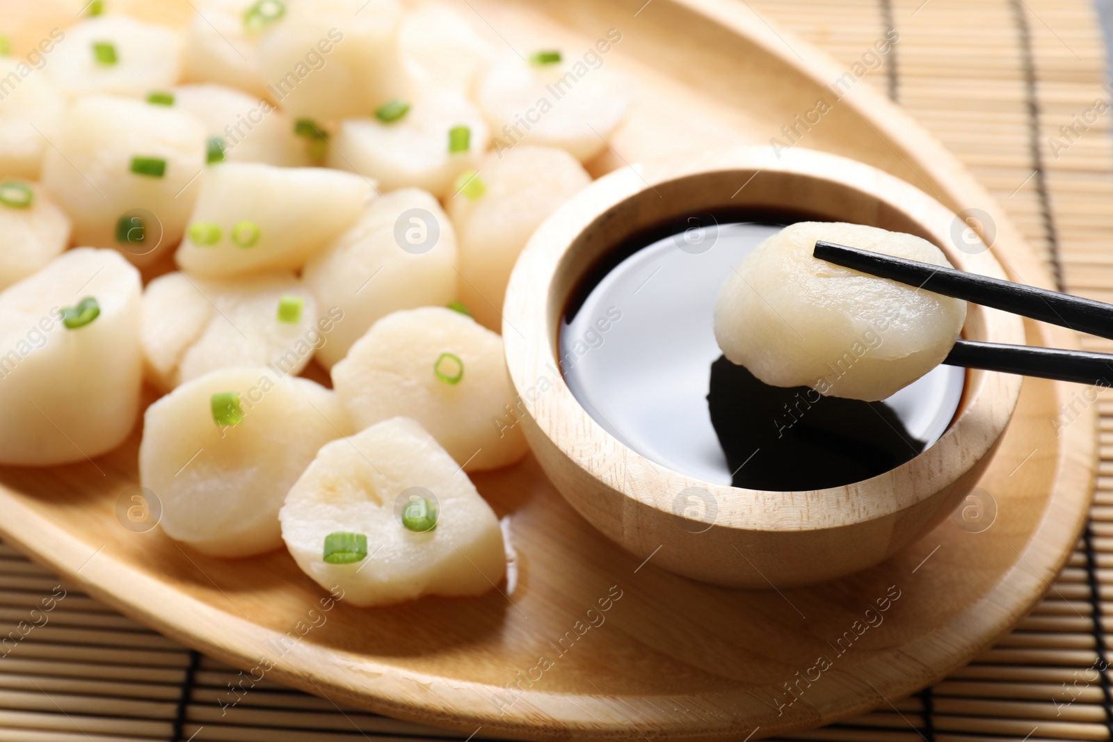 Photo of Taking raw scallop with chopsticks at bamboo mat, closeup