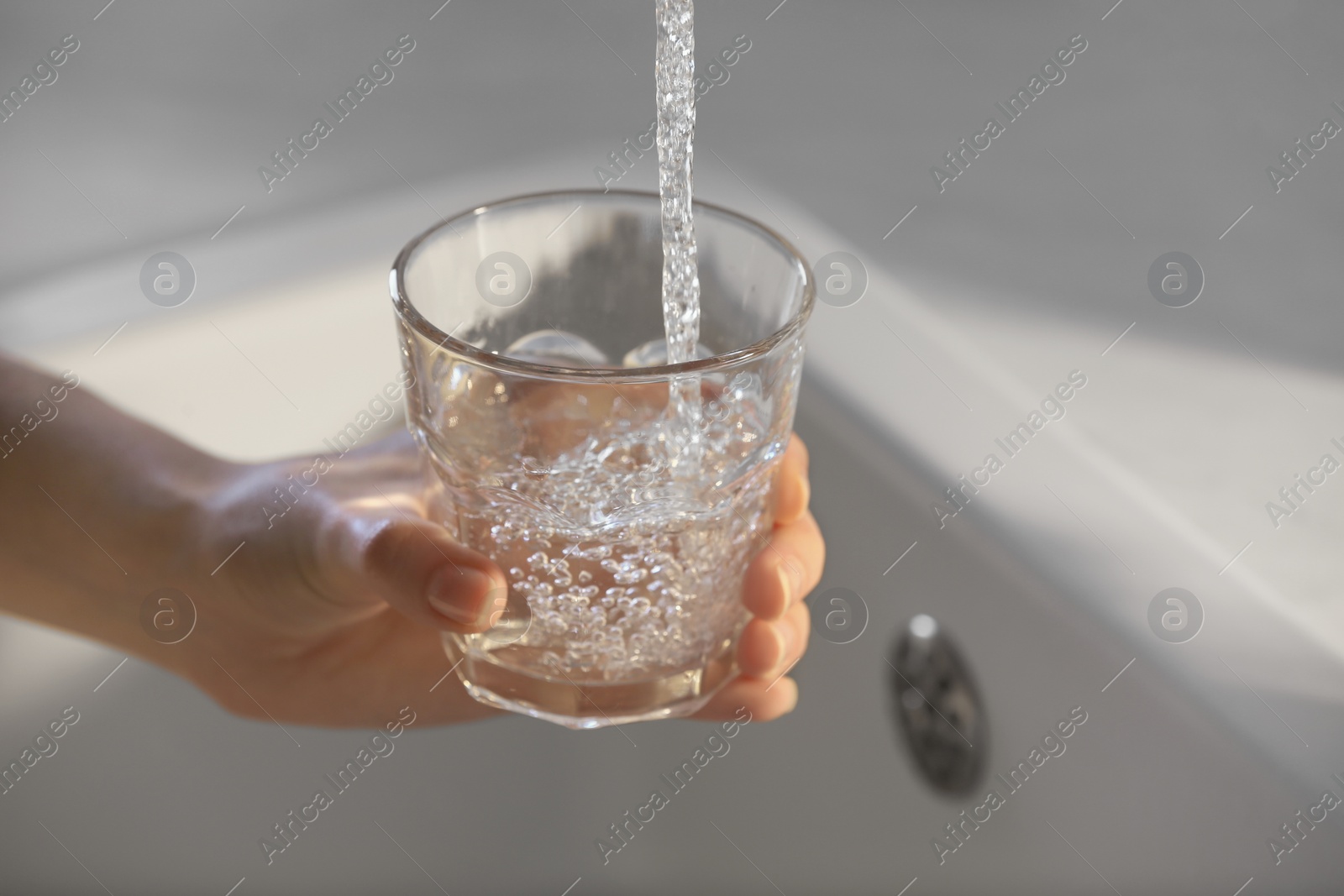 Photo of Woman filling glass with tap water from faucet in kitchen, closeup