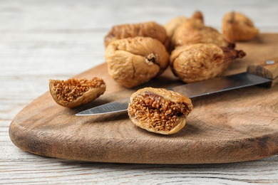 Photo of Wooden board with cut dried figs on white table, closeup