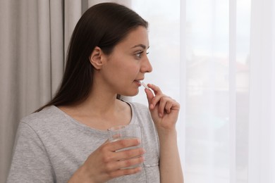 Photo of Young woman with glass of water taking pill at home