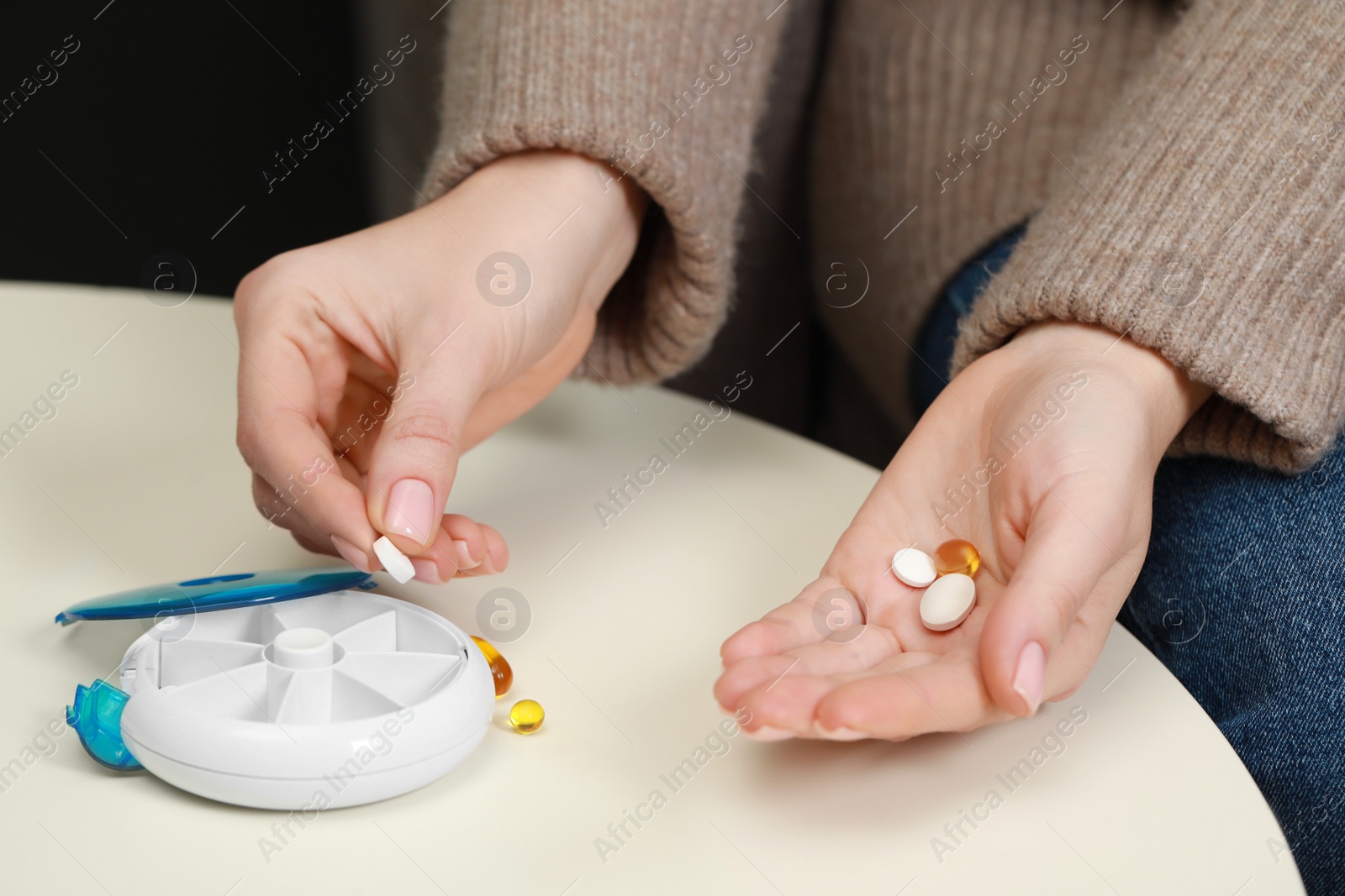 Photo of Woman taking pill from plastic container at white table, closeup