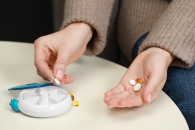 Photo of Woman taking pill from plastic container at white table, closeup