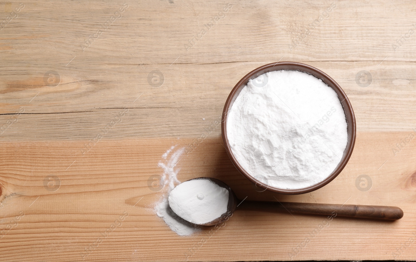 Photo of Bowl and spoon with baking soda on wooden table, top view