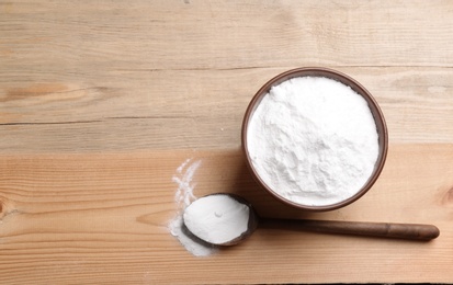 Photo of Bowl and spoon with baking soda on wooden table, top view