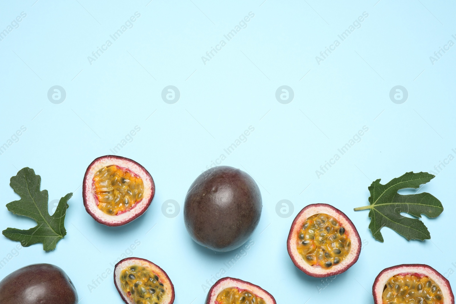 Photo of Fresh ripe passion fruits (maracuyas) with green leaves on light blue background, flat lay. Space for text