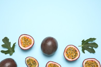 Fresh ripe passion fruits (maracuyas) with green leaves on light blue background, flat lay. Space for text