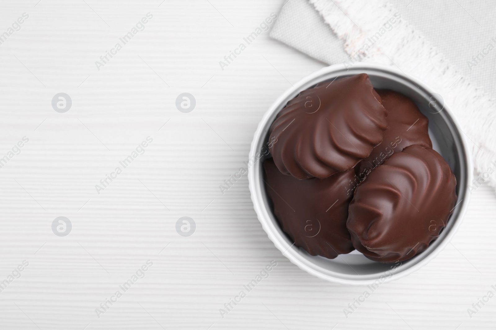 Photo of Delicious chocolate covered zephyrs in bowl on white wooden table, top view. Space for text