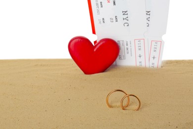 Honeymoon concept. Two golden rings, red wooden heart, tickets and sand isolated on white
