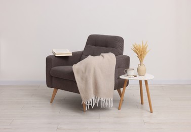 Comfortable armchair, blanket and side table near white wall indoors