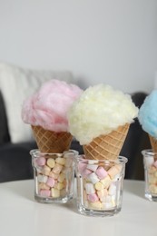 Photo of Sweet cotton candies in waffle cones and marshmallows on white table indoors