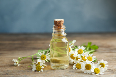 Photo of Bottle of essential oil and fresh chamomiles on wooden table