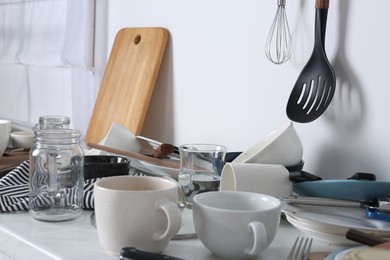 Many dirty utensils and dishware on countertop in messy kitchen