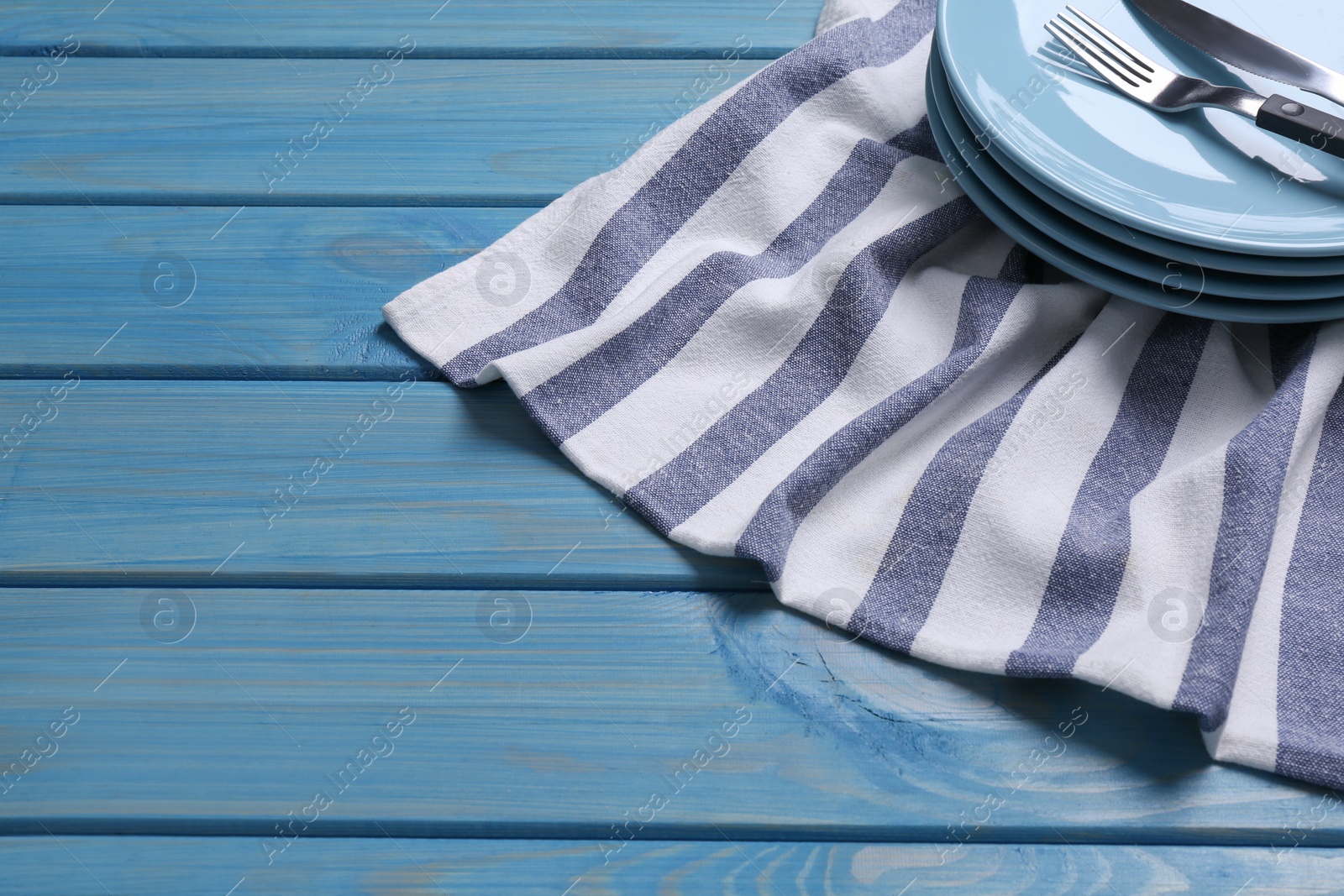 Photo of Clean kitchen towel and stack of plates with cutlery on blue wooden table. Space for text