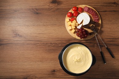 Photo of Fondue with tasty melted cheese, forks and different snacks on wooden table, top view. Space for text