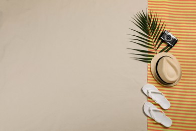 Photo of Striped beach towel, hat, camera, tropical leaf and flip flops on sand, top view. Space for text