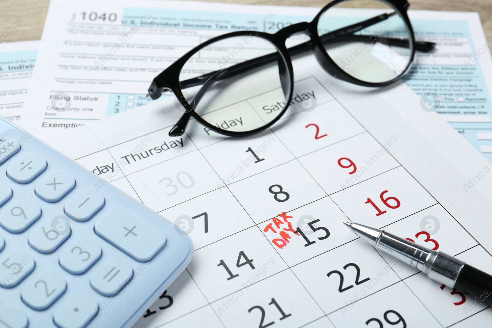 Photo of Tax day. Calendar with date reminder, documents, pen, glasses and calculator on table