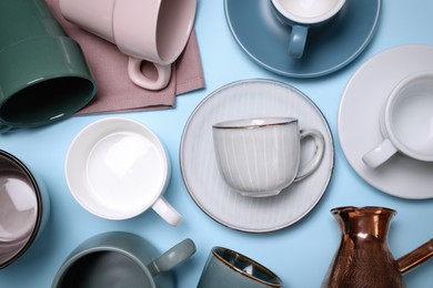 Different cups and jezve on light blue background, flat lay