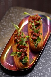 Photo of Tasty eclairs with sun-dried tomatoes and microgreens on dark table, closeup