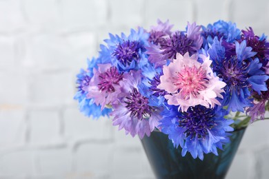 Bouquet of beautiful cornflowers in glass vase against white wall, closeup