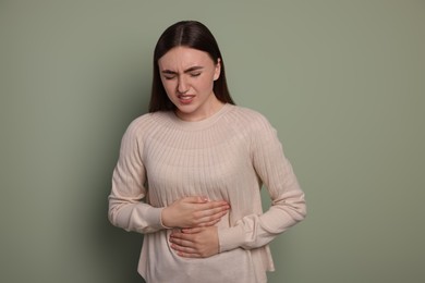 Young woman suffering from stomach pain on green background