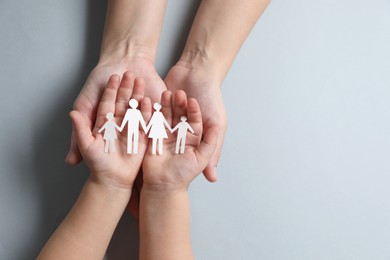 Parents and child holding paper family figures on gray background, top view. Space for text