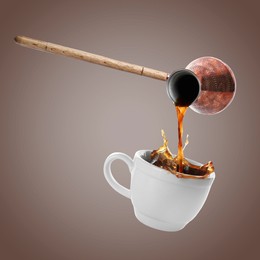 Image of Pouring freshly brewed aromatic coffee from turkish pot into cup. Objects in air on dark beige background