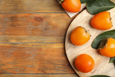Photo of Delicious fresh persimmons and green leaves on wooden table, flat lay. Space for text