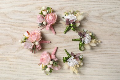 Photo of Stylish boutonnieres on white wooden table, flat lay