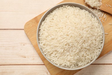 Photo of Raw basmati rice in bowl on white wooden table, top view. Space for text
