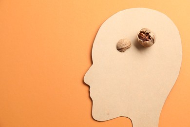 Photo of Amnesia problem. Paper cutout of human head and broken walnut on orange background, top view. Space for text